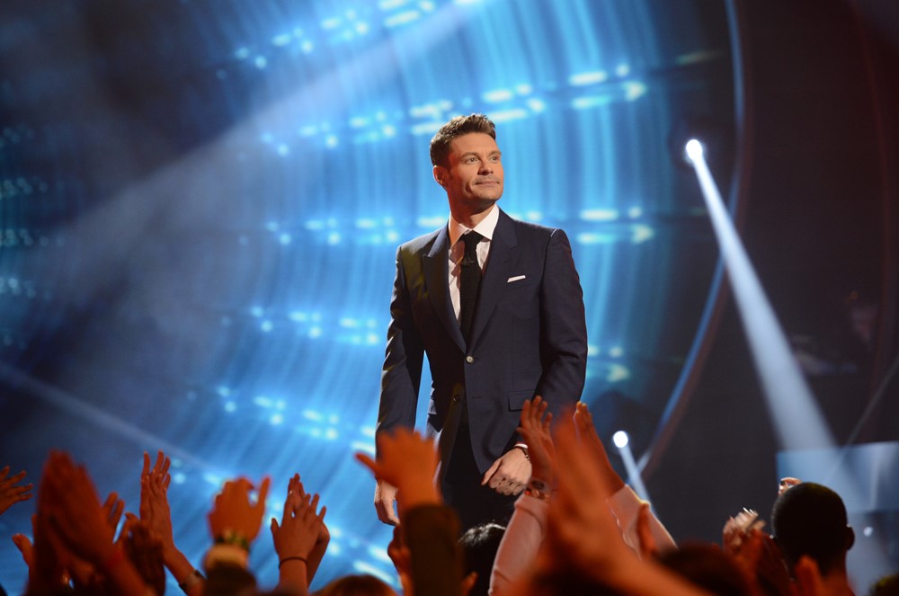 Ryan Seacrest at an event, smiling and waving at the camera